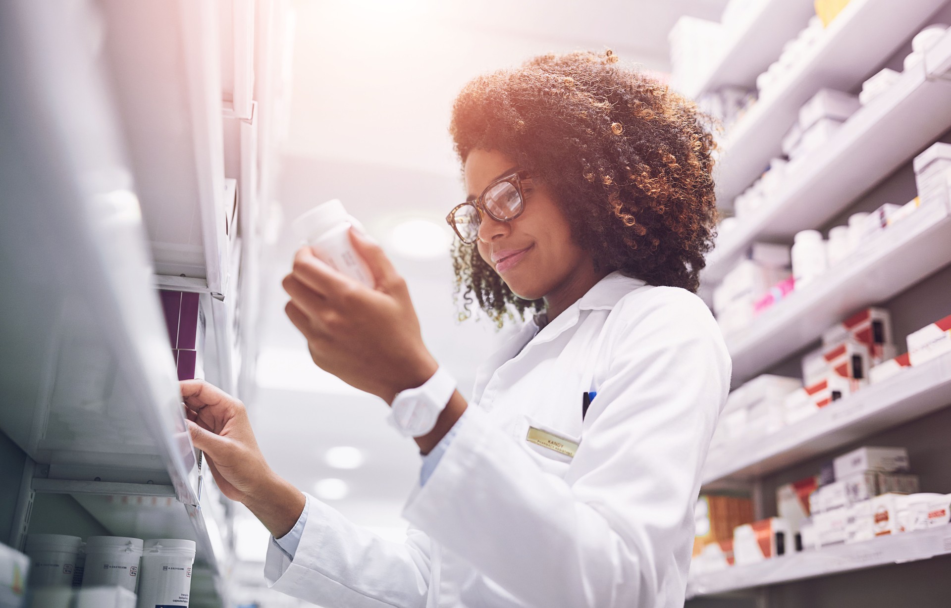 Woman, wellness and pills with pharmacy check, reading label for healthcare service or career. Female pharmacist, workplace and package inspection for inventory, prescription stock in drug store